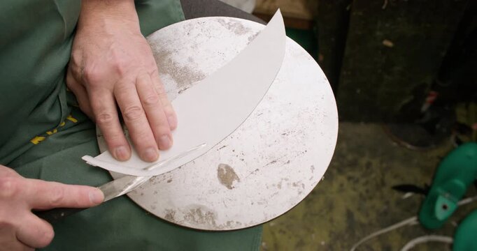 Tailor working. Craft tool. Unrecognizable professional master hands using metal knife trimming leather material for shoe manufacturing.