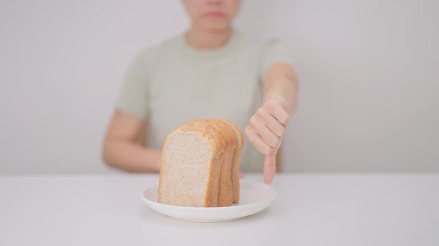 Unhappy woman showing thumbs down gesture and refusing to eat bread. concept of gluten intolerance, gluten sensitivity, carb loading concerns, or a disliking for unhealthy dietary habits