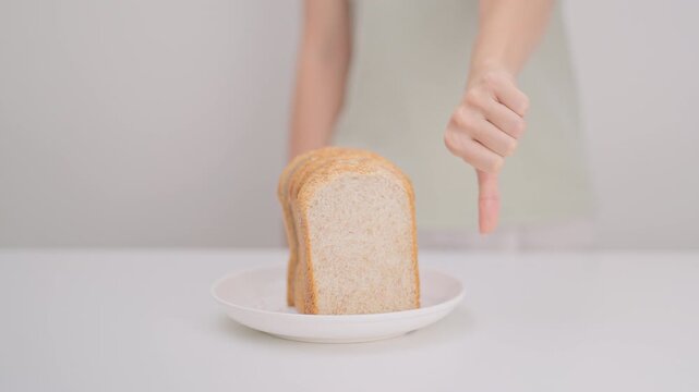 Unhappy woman showing thumbs down gesture and refusing to eat bread. concept of gluten intolerance, gluten sensitivity, carb loading concerns, or a disliking for unhealthy dietary habits