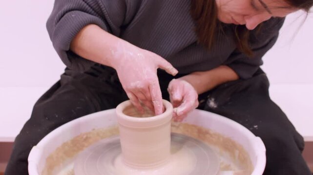 Earthenware spinning. Ceramic handmade. Professional creative woman artisan shaping clay pot using electric wheel in art workplace.