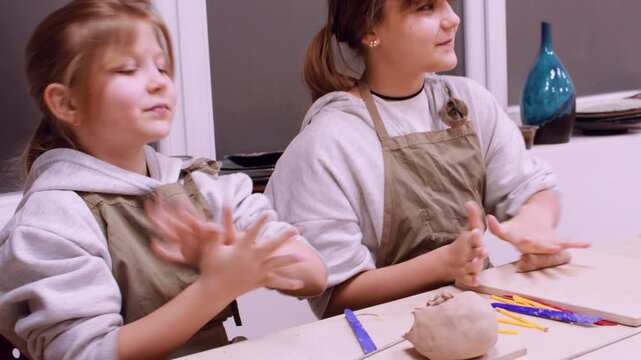 Craft education. Creative childhood. Two talented girls learning ceramic forming raw using color tool in professional artisan workplace.