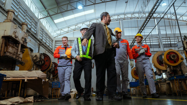 Workers and manager interact inside a factory during a team meeting in the afternoon while discussing performance and safety measures