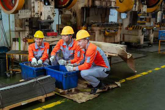 Workers are discussing tasks while sitting near blue containers in a factory