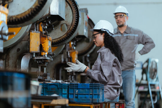 Workers are operating machinery in a factory during the day while wearing safety gear and handling materials