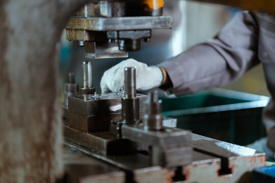 Worker operates metal stamping machine in industrial workshop during daytime