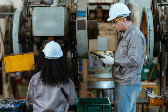 Workers are operating machinery in a factory during the day while wearing safety gear and handling materials