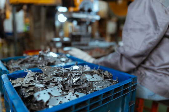 Workers handle metal parts in a factory during the daytime while sorting them in blue bins for further processing and assembly