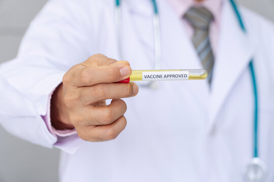 Close up of a male doctor in a white lab coat holding a test tube with a vaccine approved label. Medical professional showing successful immunization research and pharmaceutical breakthrough.
