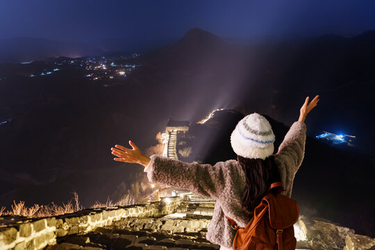 Young happy woman traveler enjoying and looking at night view of the Illuminated Great Wall of China