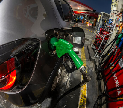 Close-up of a green fuel pump nozzle refueling a car with sugarcane ethanol biofuel at Avenida  gas station at night in downtown Marilia city. 