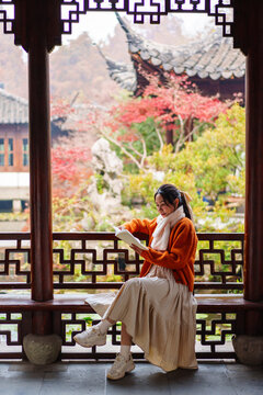 Peaceful autumn moment, A young woman sitting by a traditional Chinese carved window with colorful fall foliage.
