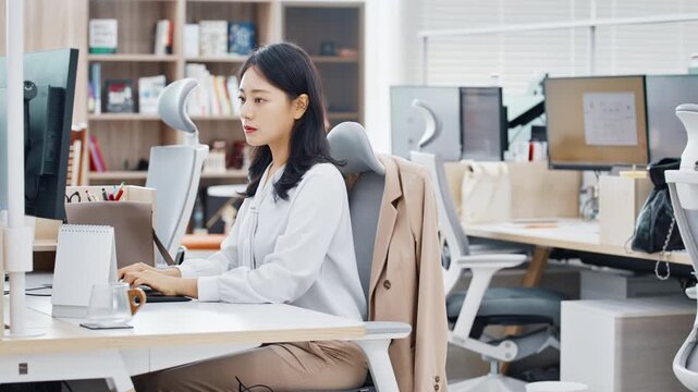 A young professional woman in a white shirt sitting at a workstation with multiple monitors in a bright modern office.