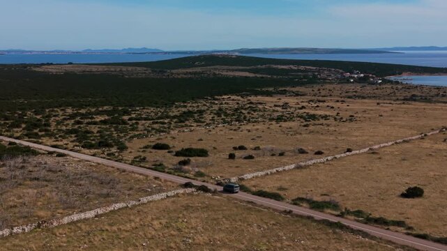 Silver van car driving through the vast wilderness of Pag Island, Croatia. Blue Adriatic Sea, aerial shot