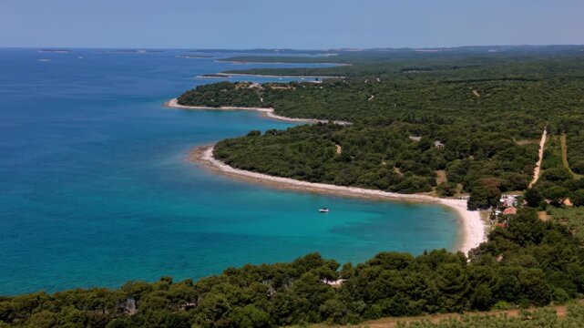Small boat anchored in a bright turquoise bay with dense green pine forest. Brijuni Islands, Croatia
