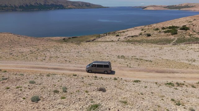 Silver van driving on a remote dirt road across the stony desert of Pag Island, Croatia. Aerial view