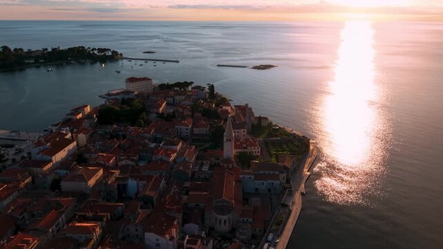 Porec old town peninsula with terracotta roofs and church tower at sunset, Istria, Croatia, aerial view.