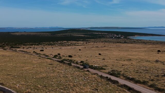 Silver van driving along a road next to a historic stone wall on Pag Island, Croatia. Aerial view.