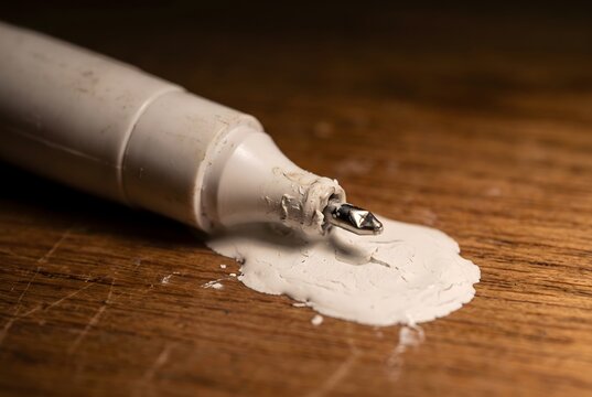Macro close up of a crushed correction pen leaking a thick puddle of white fluid