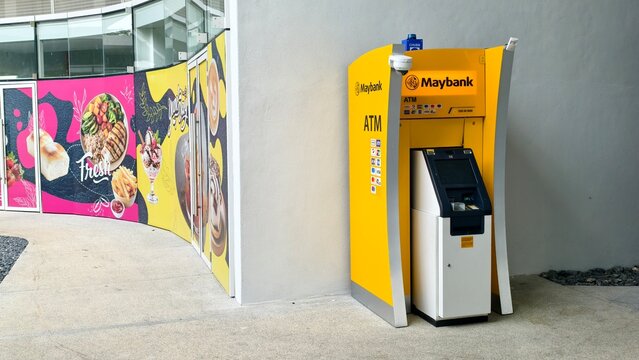 Ipoh,Malaysia - 22 July 2026: Side angle view of a yellow Maybank ATM machine next to colourful store hoardings.