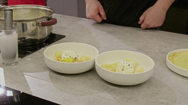 Unrecognizable male chef presenting two bowls of dessert with ice cream during culinary workshop with child student. Footage ideal for cooking school promos and food industry advertisements