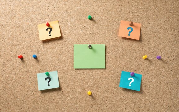 Colorful sticky notes with question marks pinned on a textured brown cork office bulletin board