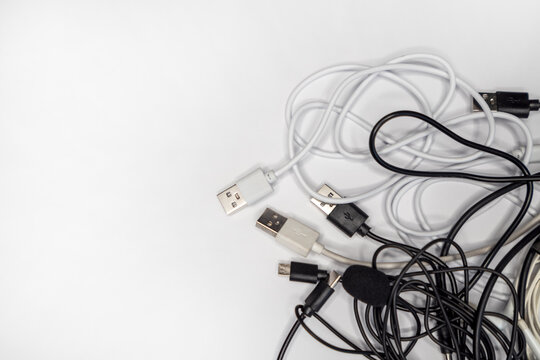 Various tangled USB cables on a white background, showcasing different types and colors of connectors for charging and data transfer.