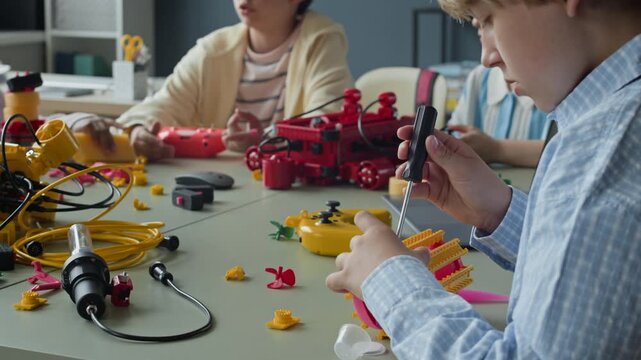 Caucasian boy assembling robotic toy with screwdriver during STEM lesson with classmates in background. Footage is ideal for promoting kids science camps and modern school education programs