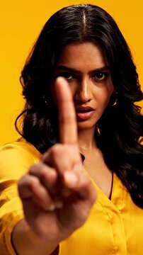 Serious young woman gesturing stop against a yellow background
