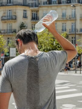Man pouring water on himself to cool off in sunny city street