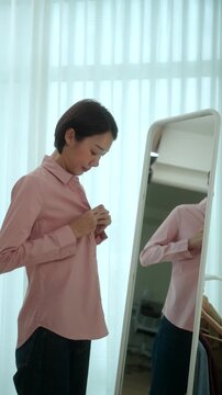 Woman getting dressed in front of a mirror in a modern dressing room. Morning routine capsule wardrobe, personal styling, fashion confidence. Self-care and everyday lifestyle concept.
