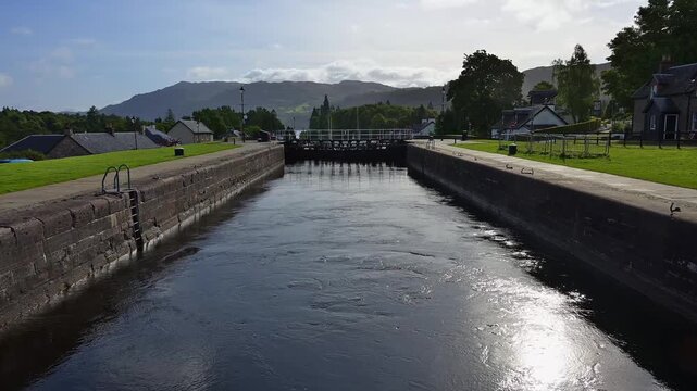 Ein gepflasterter Kanalbereich mit Blick auf Geb&auml;ude und Berge unter klarem Himmel, Kaledonischer Kanal, Fort Augustus, Loch Ness, Schottland, Vereinigtes K&ouml;nigreich, Gro&szlig;britannien