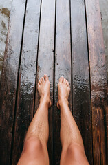 Fototapeta premium Unshod feet rest on a soggy wooden boardwalk. Two individuals' legs, with one knee lower than the other, skim wet planks near the water. Summertime leisure by the pier.