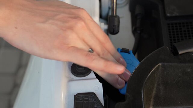Male hand closes the windshield washer fluid reservoir cap under the hood of a modern car. Close-up of routine vehicle maintenance, automotive service and preparation for refilling washer fluid.