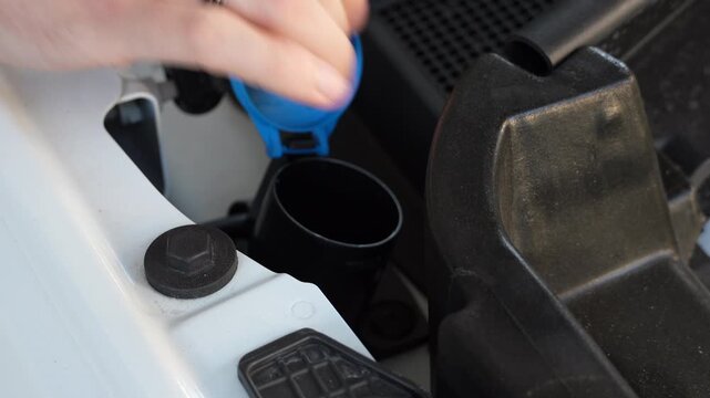 Male hand opens the windshield washer fluid reservoir cap under the hood of a modern car. Close-up of routine vehicle maintenance, automotive service and preparation for refilling washer fluid.
