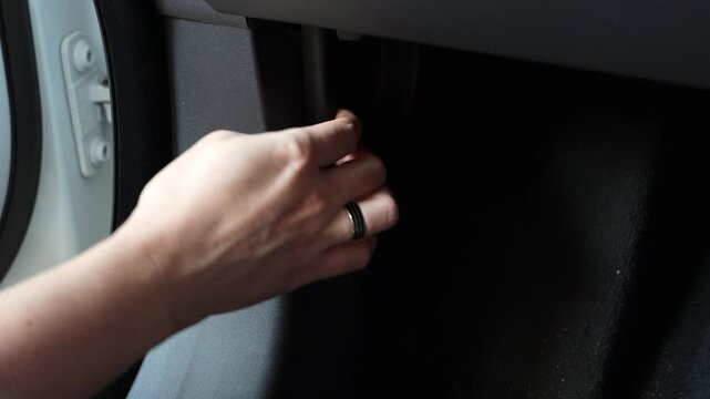 Male hand pulls the trunk release lever located beneath the steering wheel inside a modern luxury car. Close-up of the interior control used to unlock the luggage compartment during everyday vehicle o