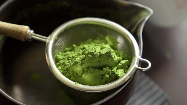 Sifting vibrant green matcha tea powder through fine mesh strainer into ceramic bowl for traditional preparation.