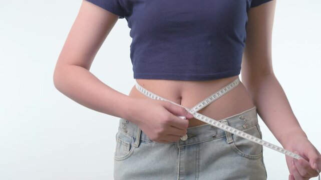 Proud motivated woman tracking body progress uses white tape measure around slim waist during healthy weight loss journey with determination