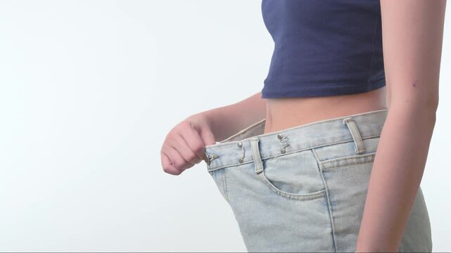 Proud slim woman shows waist success in loose denim jeans during healthy weight loss journey celebrating body fitness progress