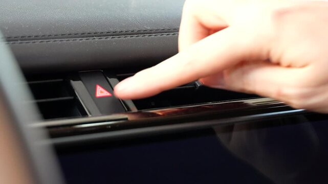 Male hand presses the hazard warning button to switch off emergency flashers inside a modern luxury vehicle. Close-up of automotive controls, dashboard buttons and safe driving operation.