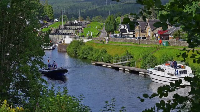 Boote liegen am Flussufer in einer h&uuml;geligen Landschaft mit vereinzelt stehenden H&auml;usern, Kaledonischer Kanal, Fort Augustus, Loch Ness, Schottland, Vereinigtes K&ouml;nigreich, Gro&szlig;britannien