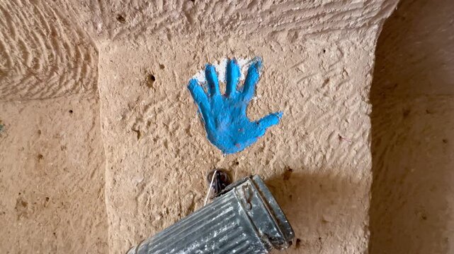 Bright blue painted handprint representing Hand of Fatima on a rough clay pillar in Traditional Matmata cave house in Tunisia.