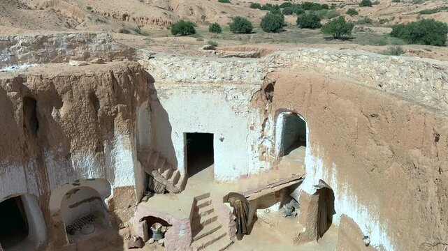 Sunlit courtyard of a traditional Matmata troglodyte cave house with carved stairs, doorways and arid hills around, Tunisia.