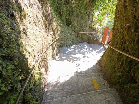 A narrow concrete staircase descends between two mossy walls. Blue and yellow arrows mark a clear path forward.
