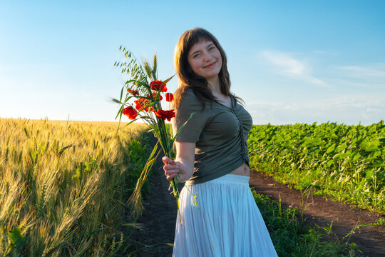 Young woman holding bouquet of red poppies in wheat field