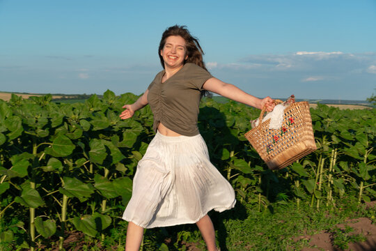 Happy young woman jumping in sunflower field with wicker basket