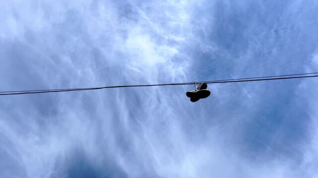 Pair of small boots hanging on overhead wire against cloudy blue sky