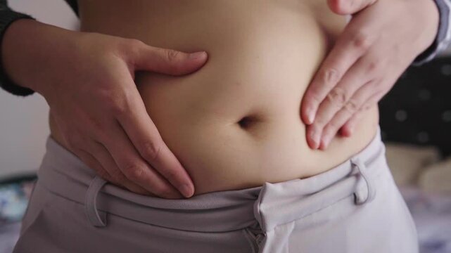 Close-up of a person holding their stomach with both hands, conveying bloating, abdominal discomfort and digestive issues