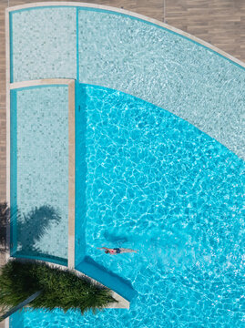 Young girl swimming in clear blue pool during sunny summer vacation. This aerial view captures family,  friends, fun, and recreation at resort, relaxation and joyful outdoor moments.