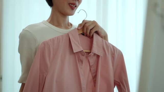 Close-up Woman choosing and trying on clothes in front of a mirror at home. Outfit selection. Capsule wardrobe, personal styling, sustainable fashion. Self-confidence and morning routine concept.
