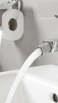 White ceramic bidet at modern restroom. Water is running. Nobody. Vertical footage